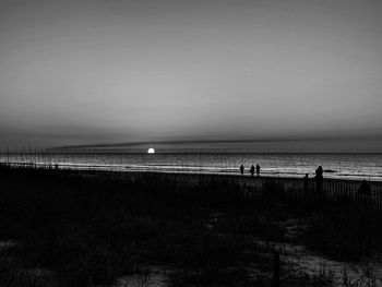 Silhouette people on beach against clear sky