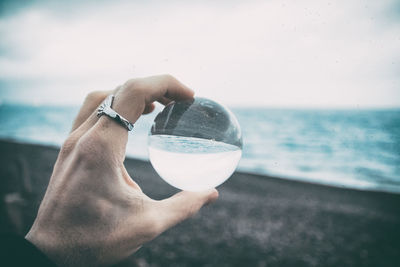 Cropped hand holding crystal ball at beach