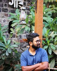 Young man looking away while standing against plants