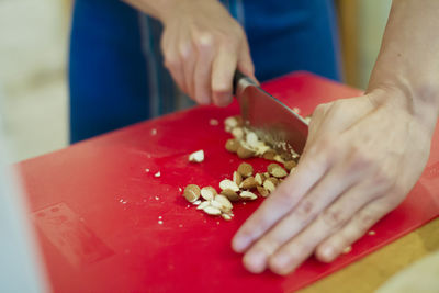 Midsection of person chopping almonds on red cutting board