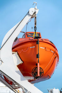 Vertical shot of orange life boat hanging on a crane onboard sailing ocean ship 
