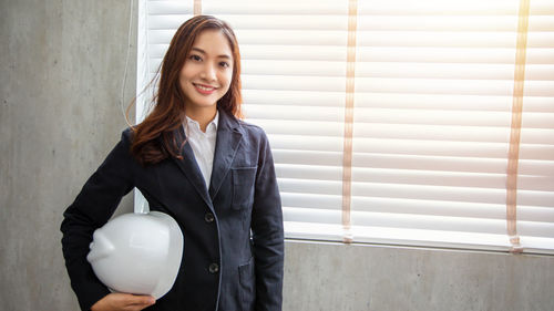 Portrait of young woman standing by window at home