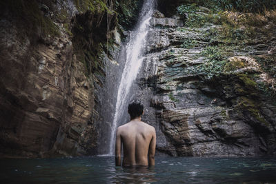 Rear view of shirtless man standing at waterfall