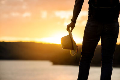 Man holding umbrella against sky during sunset