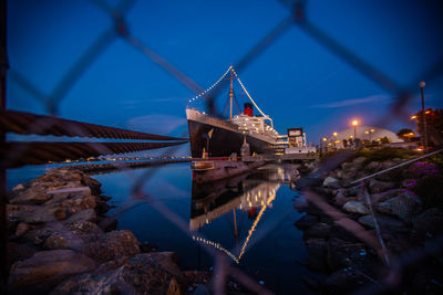 Ship at harbor against sky at night seen through fence