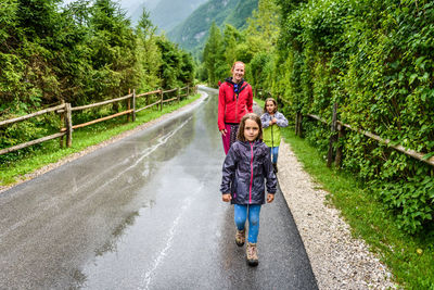 Full length of family walking on wet road amidst trees