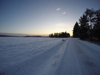 Snow covered road against sky during sunset