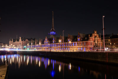 Illuminated buildings by river against sky at night