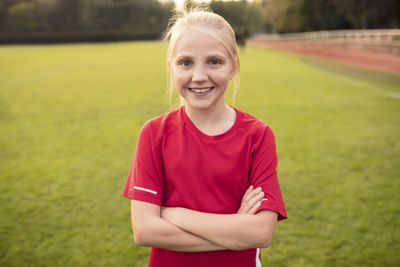 Portrait of happy girl wearing red t-shirt standing with arms crossed on soccer field