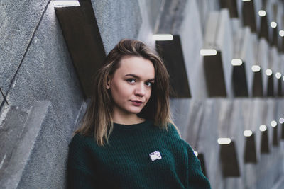 Portrait of beautiful young woman standing against wall outdoors