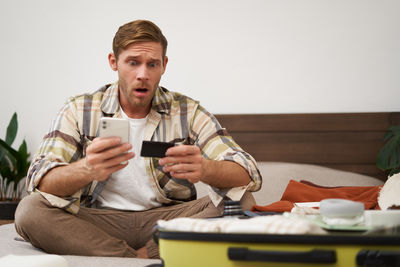 Portrait of young man using mobile phone while sitting at home