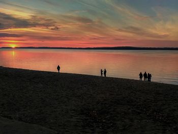 Silhouette people standing on beach against sky during sunset