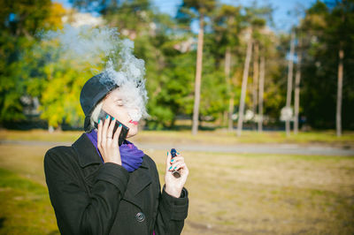 Young woman talking on mobile phone while smoking at park