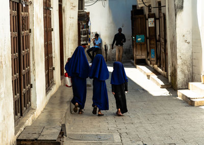 Rear view of people walking on footpath amidst buildings