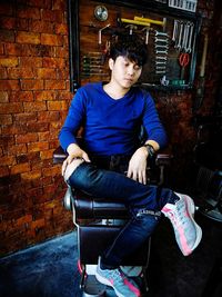 Young man sitting on chair against wall