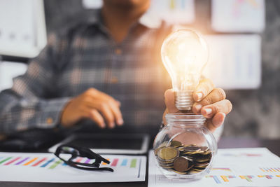 Midsection of man holding light bulb on table