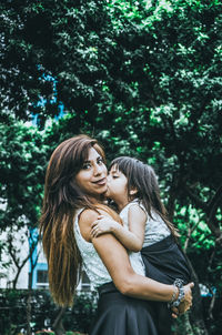 Portrait of woman carrying daughter against trees