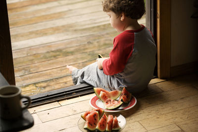 Boy sitting on doorway by watermelons in plates