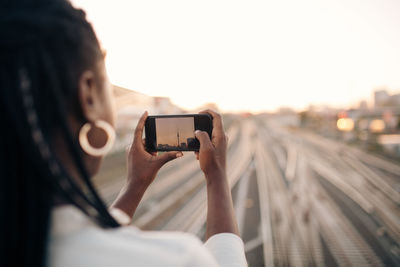 Young woman photographing fernsehturm through mobile phone during sunset