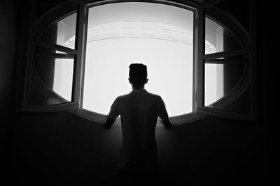 Rear view of silhouette boy standing in window