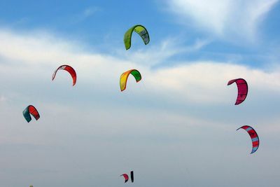Low angle view of people paragliding against sky