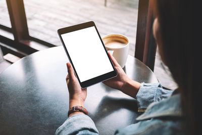 Cropped hand of woman holding digital tablet sitting at cafe