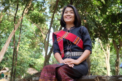 Smiling woman in traditional clothing sitting against trees