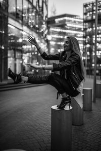 Young woman crouching on bollard in city at night