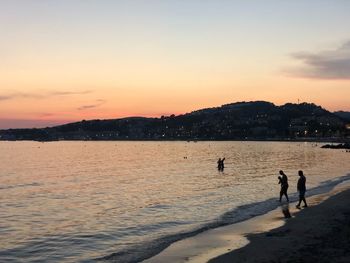 People at beach against sky during sunset