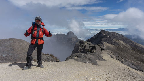 Young man climber standing on the summit of guagua pichincha volcano wearing red coat and helmet