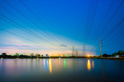 Scenic view of illuminated city by river against sky at dusk