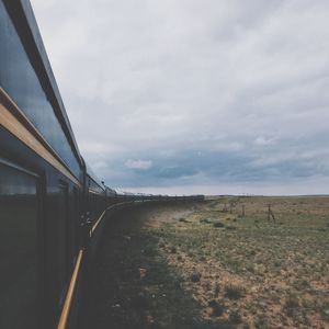 Train passing by field against cloudy sky