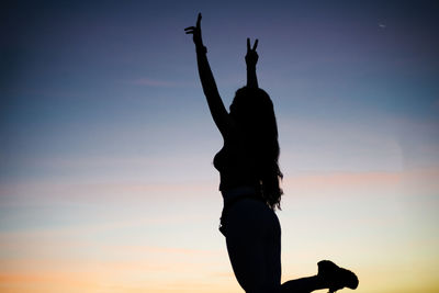 Silhouette woman with arms raised standing against sky during sunset