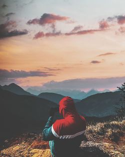 Rear view of woman standing on mountain against sky during sunset