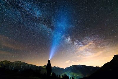 Rear view of silhouette person standing by mountains against star field