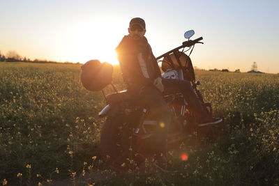 Man riding motorcycle on field against sky during sunset