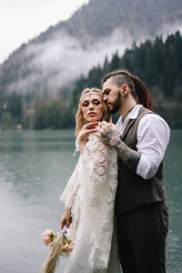 Two happy people in love the bride and groom in wedding outfits embrace by the lake and mountains