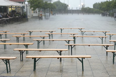 Empty chairs and tables at sidewalk cafe in rain