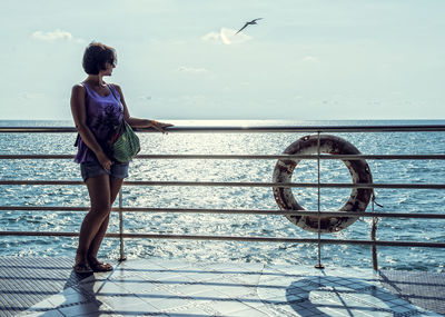 Woman standing by railing on boat deck against sky