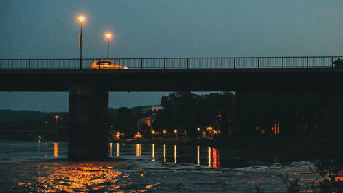 Illuminated bridge over river against sky at dusk