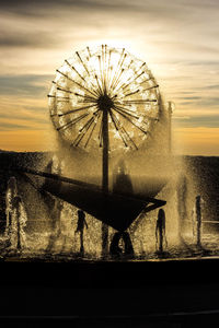 Silhouette people by ferris wheel against sky during sunset