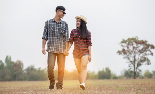 Young couple holding hands while walking on field against sky