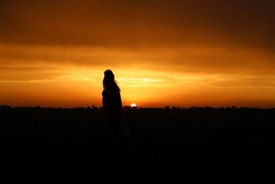 Silhouette woman on field against orange sky during sunset