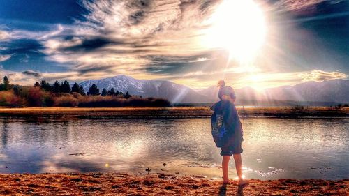 Rear view of woman standing by lake against sky during sunset