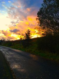 Road by trees against sky during sunset