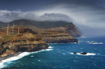 High angle view of rocky coastal feature against clouds