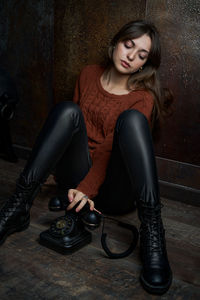 Portrait of young woman with telephone sitting on floor