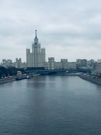 View of buildings by river against cloudy sky