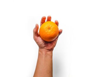 Cropped image of hand holding orange against white background
