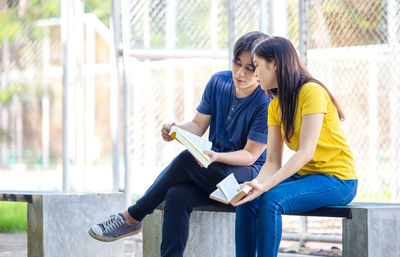 Couple of students are studying together, and a teenager sits on a seat beside court with a book.